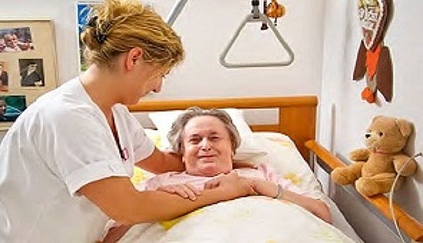 Das Bild zeigt eine Mitarbeiterin mit einer Bewohnerin, die im Bett liegt